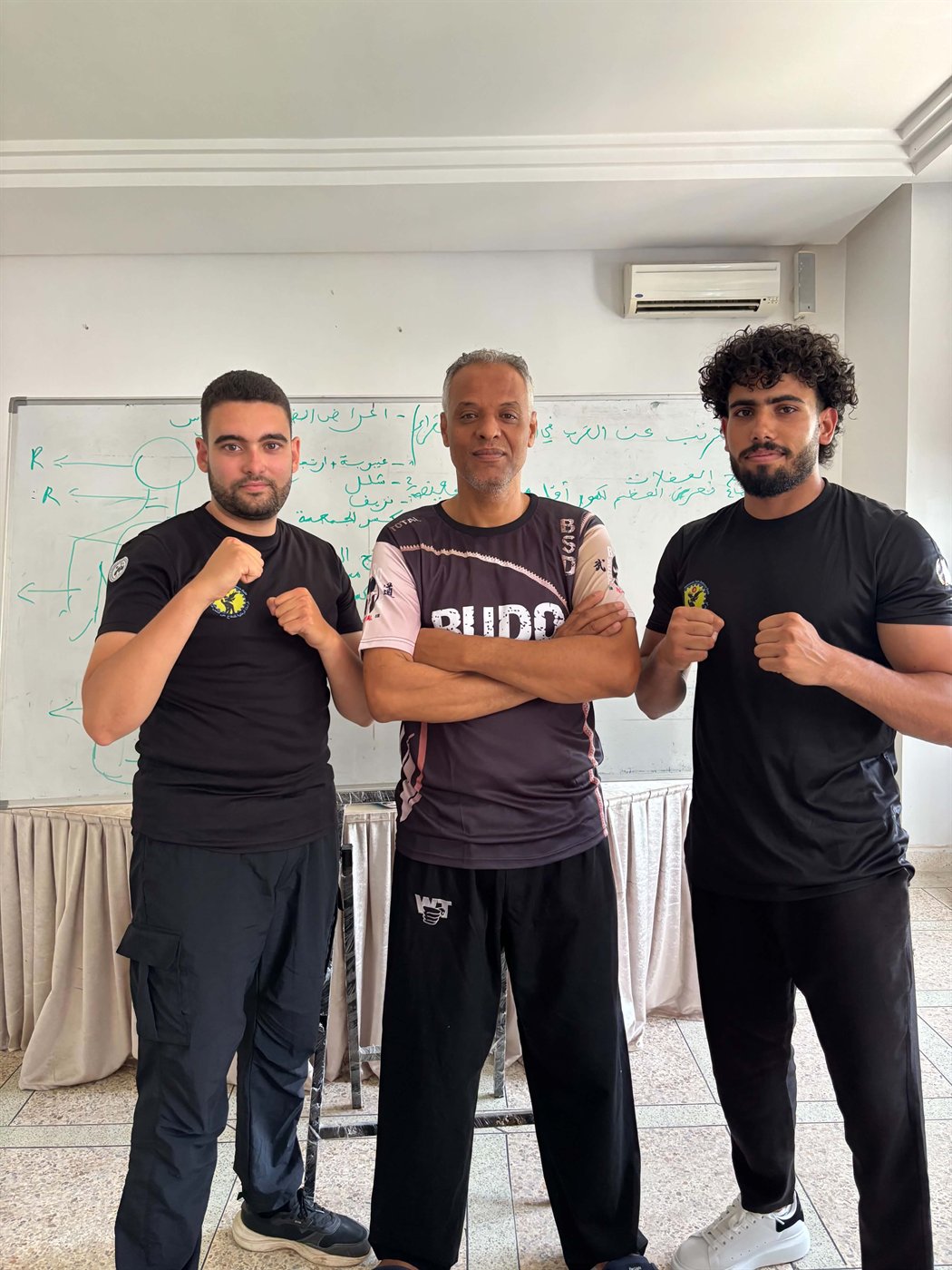 Three martial arts instructors standing together with raised fists during training