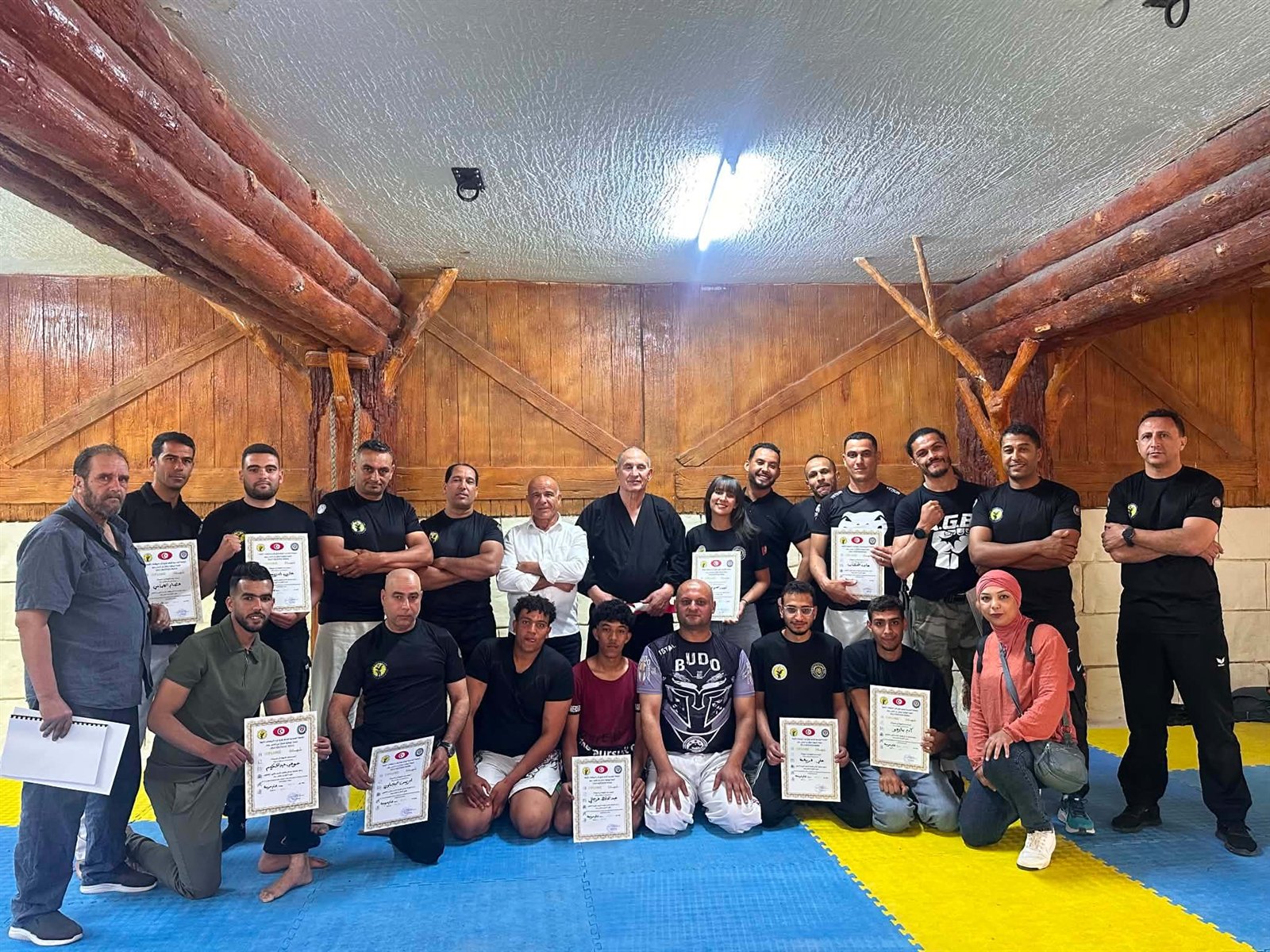 Large martial arts team posing with certificates inside a dojo